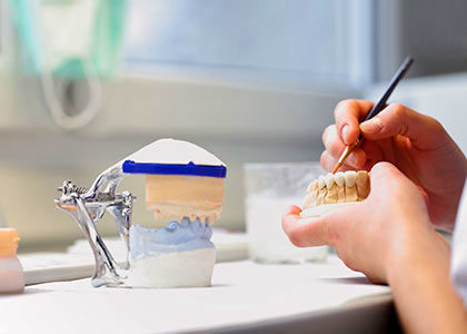 A denturists hands working on the finishong touches of a lowe denture over a workbench at the Toronto Denture Centre