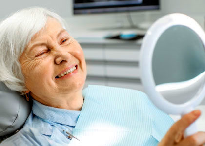 A denture patient looking in a mirrior and smiling her new dentures